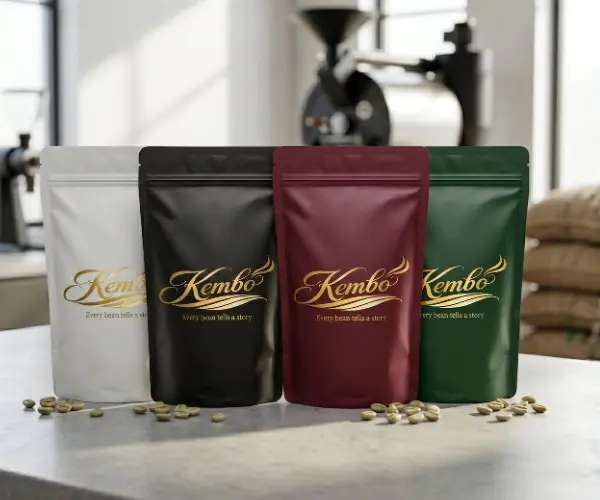 Four Kembo coffee bags in brown, green, black, and burgundy with gold branding, arranged side by side on a rustic wooden surface with coffee beans